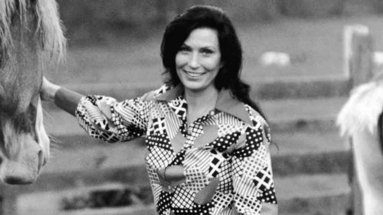 Loretta Lynn smiling outside with hand on a horse