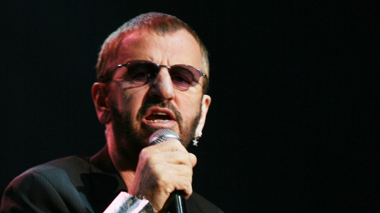 Ringo Starr looking shocked while singing into a microphone on stage