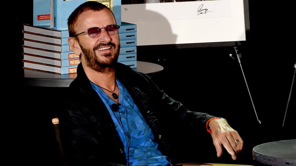 Ringo Starr smiling in front of stack of books