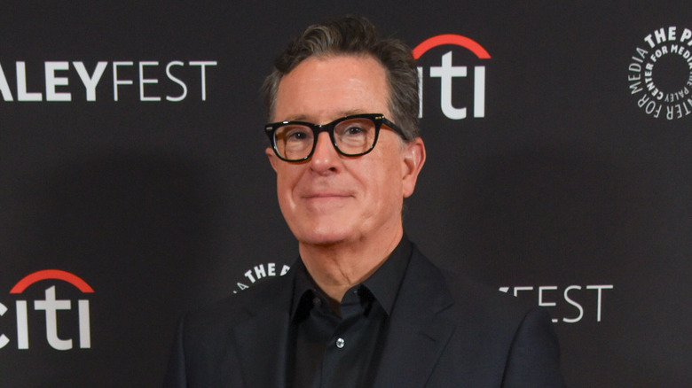 Stephen Colbert posing in front of a black Paleyfest banner