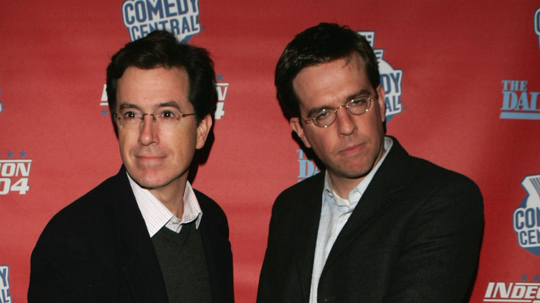 Stephen Colbert and Ed Helms posing in front of a red Comedy Central background