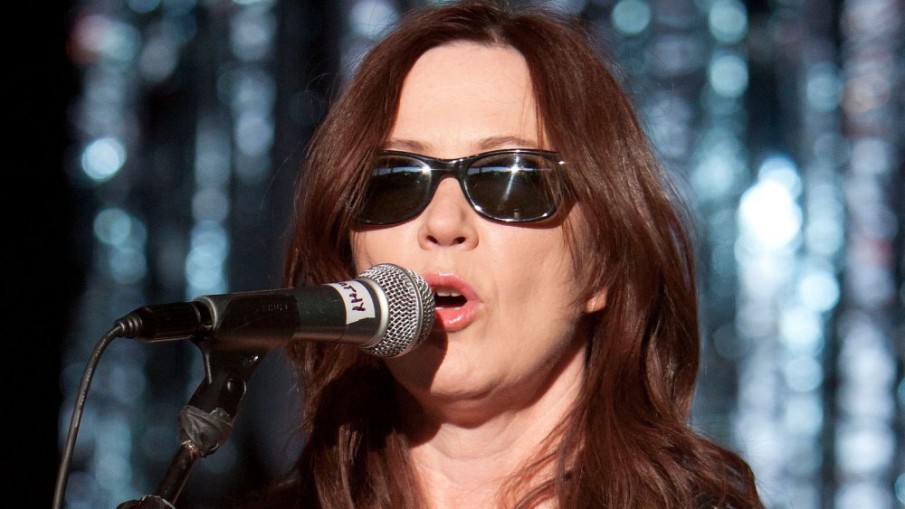 Kathy Valentine with sunglasses singing into mic on stage