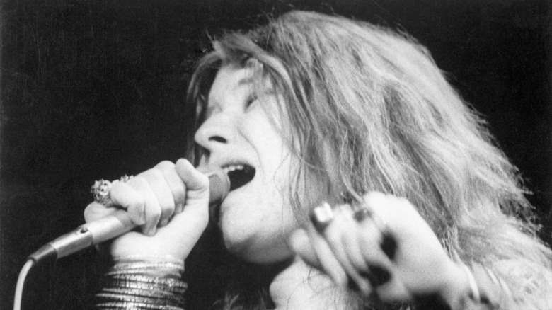 Janis Joplin singing into microphone with lots of bangles on her arm