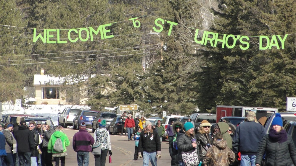 Crowd walking in a town street under a Welcome to St. Urho's Day banner