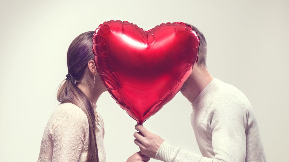 A couple shares a kiss hidden by a heart-shaped Valentine's Day balloon