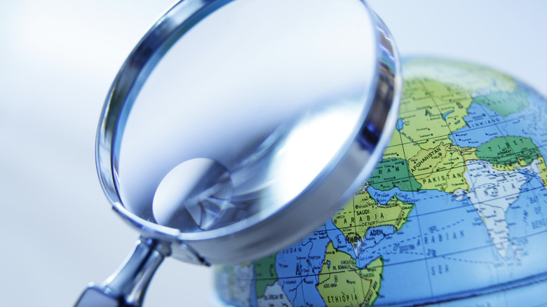 A magnifying glass in front of a globe that is rotated to show Africa and Asia