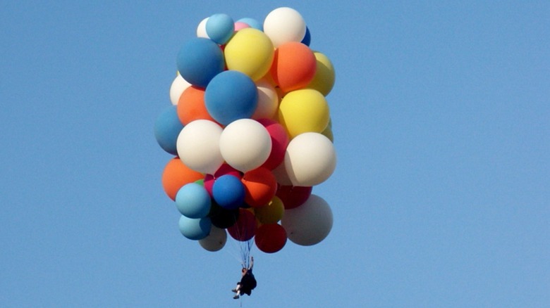 Helium balloons floating while attached to chair with person sitting in it