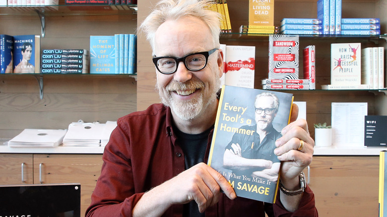 Adam Savage holds up his book and smiles