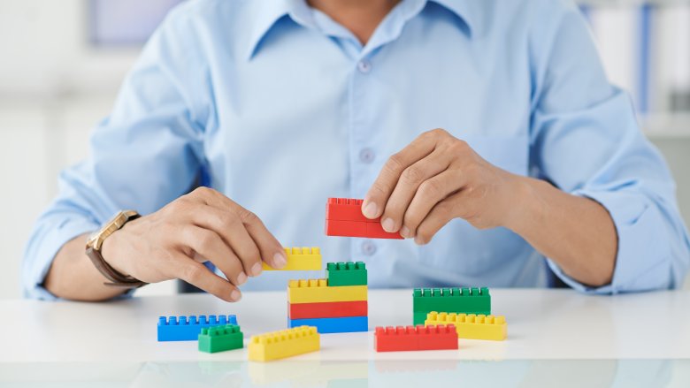 Person in blue shirt at white table playing with lego