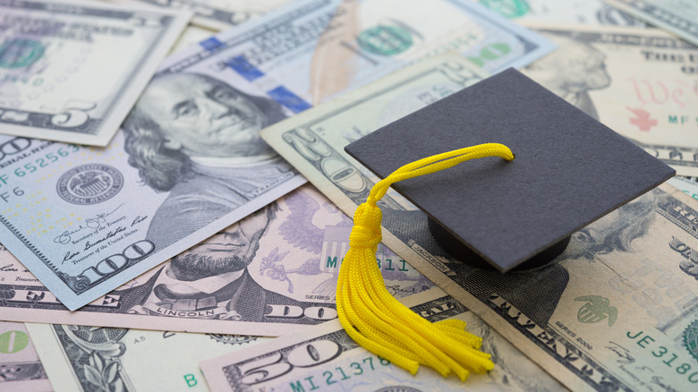 mortar board with yellow tassel on top of paper dollar bills