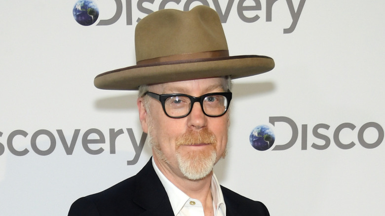 Adam Savage with goatee and glasses wearing hat and suit at Discovery event
