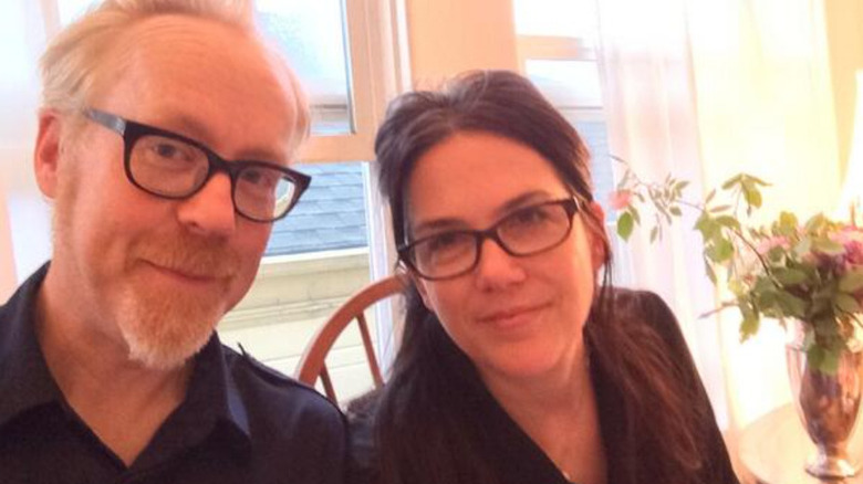 Adam Savage with goatee and glasses and his wife smiling indoors