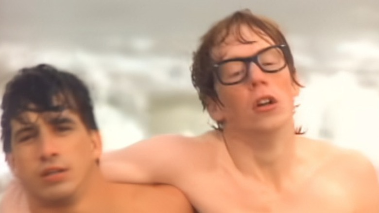 Adam Savage shirtless in glasses being helped out of water in Billy Joel music video