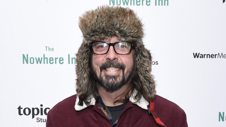 Dave Grohl smiling in glasses, red sweater, and furry trapper hat at event