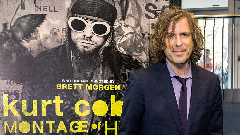 Brett Morgen stood smiling in suit by poster for Montage of Heck