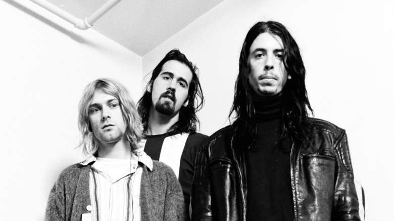 Three Nirvana bandmembers stood together looking solemn
