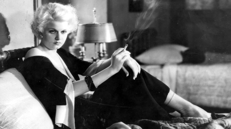 Jean Harlow seated, smoking sadly