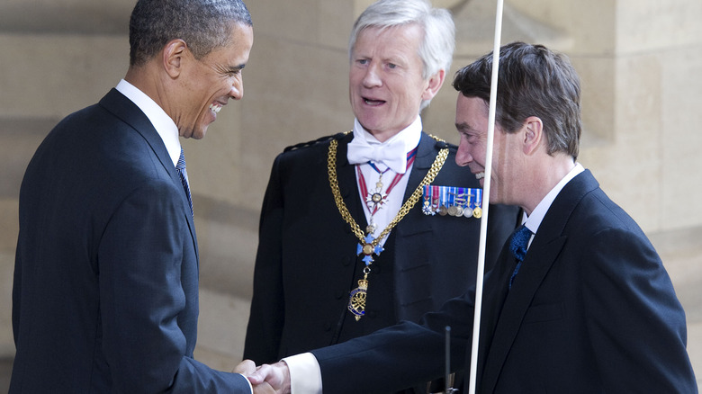 The lord chamberlain holds his staff while greeting President Barack Obama