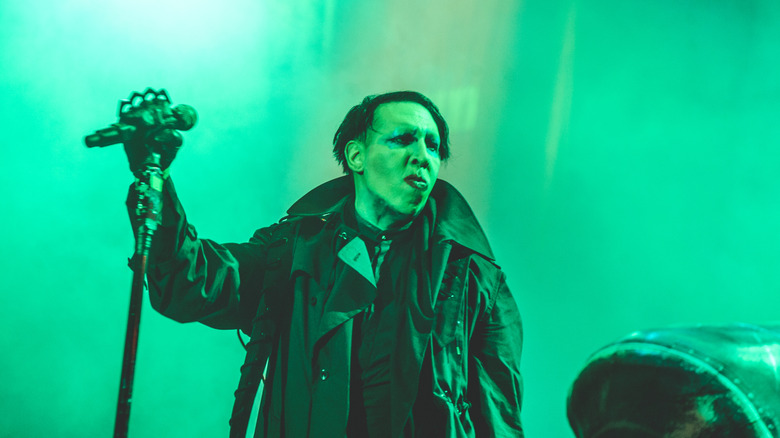 Manson looking forlorn in leather jacket holding mic lit in green onstage