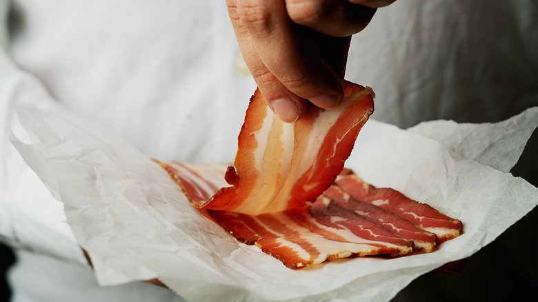 bacon on white paper being lifted by hand