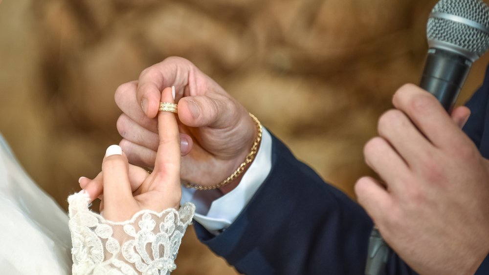 hands of jewish groom putting ring on finger of bride