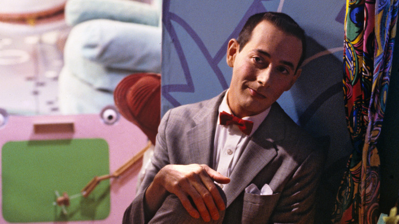 Paul Reubens sitting against a wall as Pee-wee Herman
