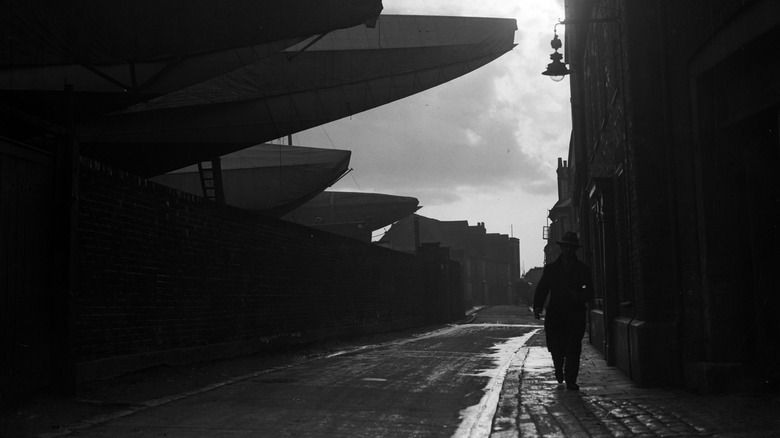A man walks down Gosport Boatyard as ships loom over him.
