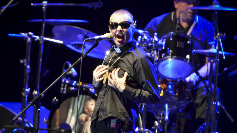 Sinéad O'Connor onstage in priest outfit and sunglasses