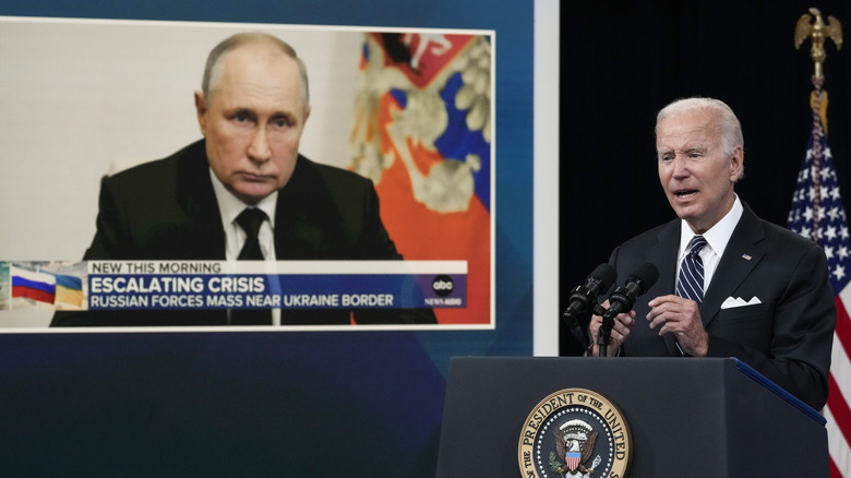 President Biden speaks with Vladimir Putin on a screen behind him.