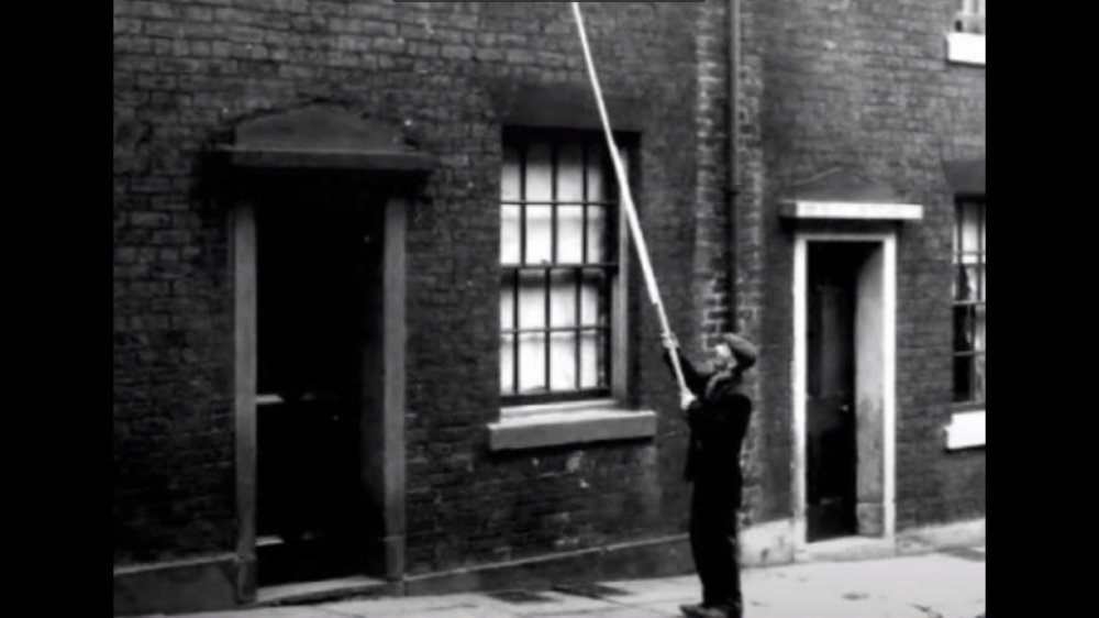 A knocker upper on a wakeup call with a long stick