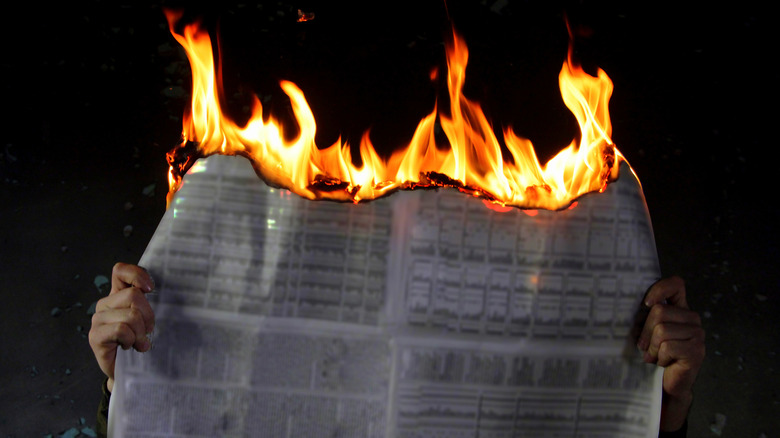 hands holding burning newspaper