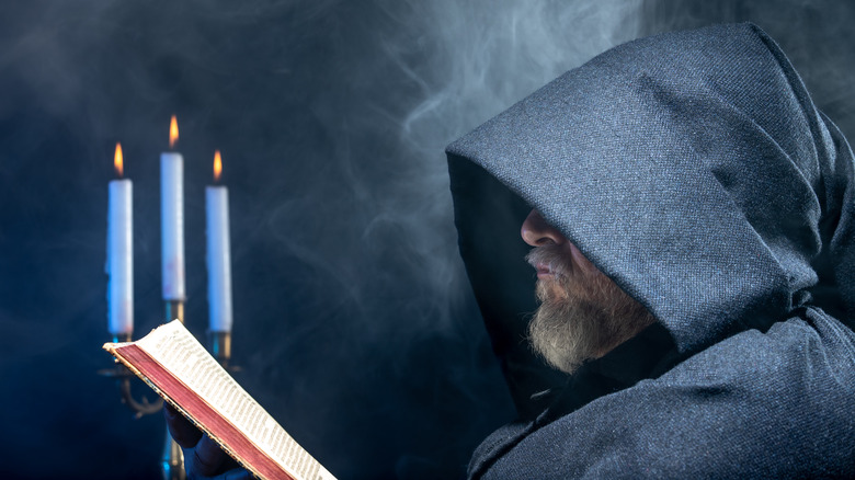 Hooded man reading a Bible with candles