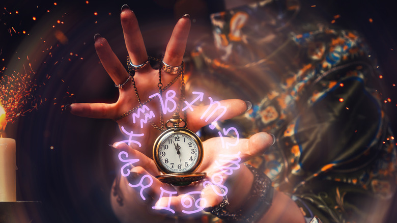 Hands holding watch with astrological symbols around