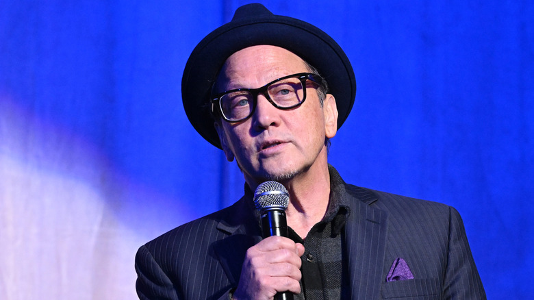 Rob Schneider in hat speaking into microphone