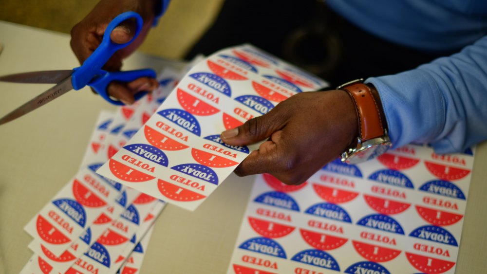 A volunteer cuts out " I VOTED TODAY" stickers for voters queueing outside of a satellite polling station on October 27, 2020 