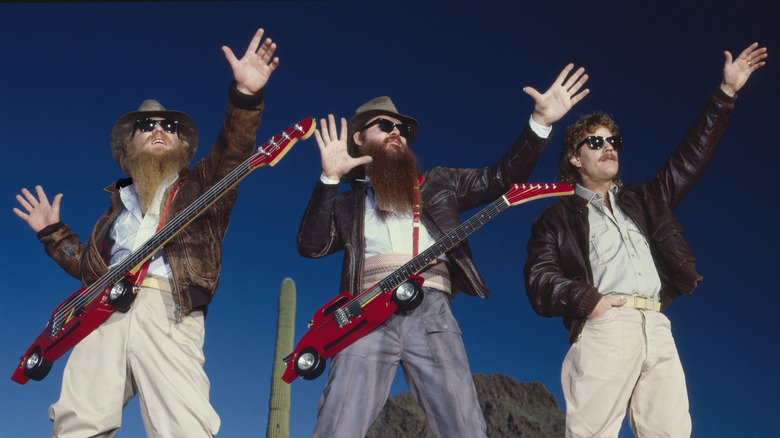 ZZ Top posing with guitars and raised hands