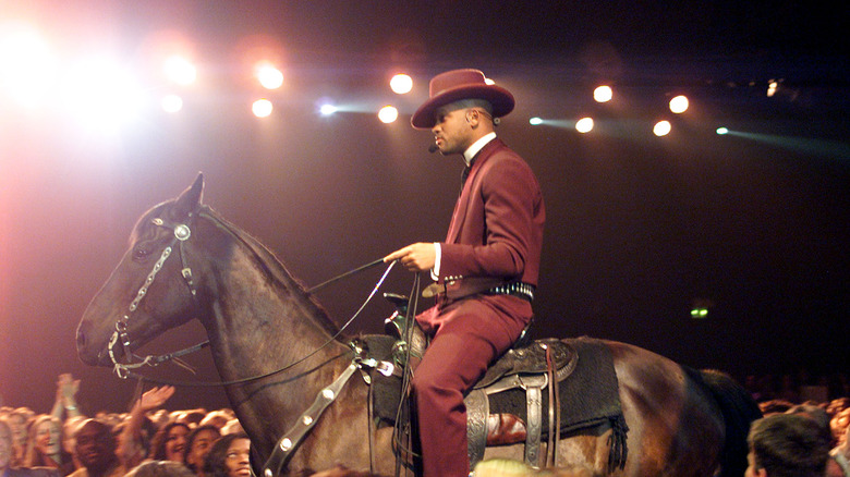 Will Smith riding a horse in purple wild west suit and hat