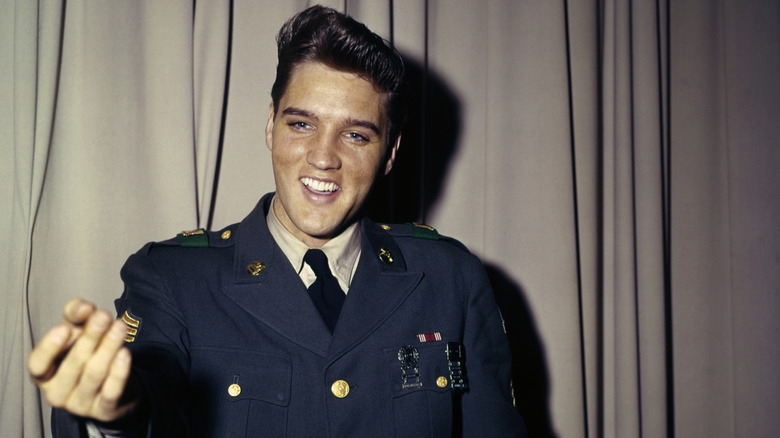 Elvis Presley smiling in front of a curtain in his army uniform