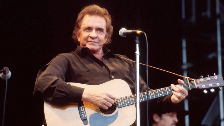 An elderly Johnny Cash strumming a guitar on stage
