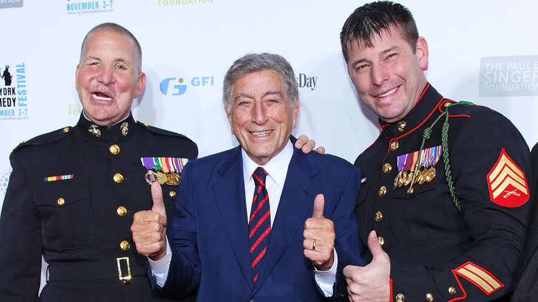 Tony Bennett giving a double thumbs up with two servicemen on the red carpet at a benefit