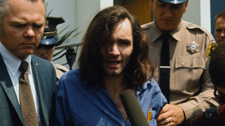 Charles Manson with police speaking into microphone