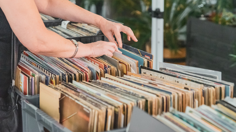 A pair of hands leafing through crates of vinyl records in an outdoor setting.