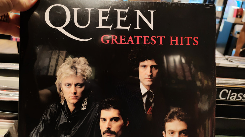 hand pulling Queen greatest hits album out of record stacks
