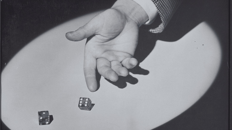 Black and white image, spotlight on hand throwing pair of dice