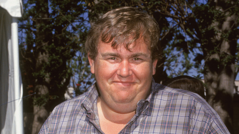 John Candy smiling outdoors in checkered shirt