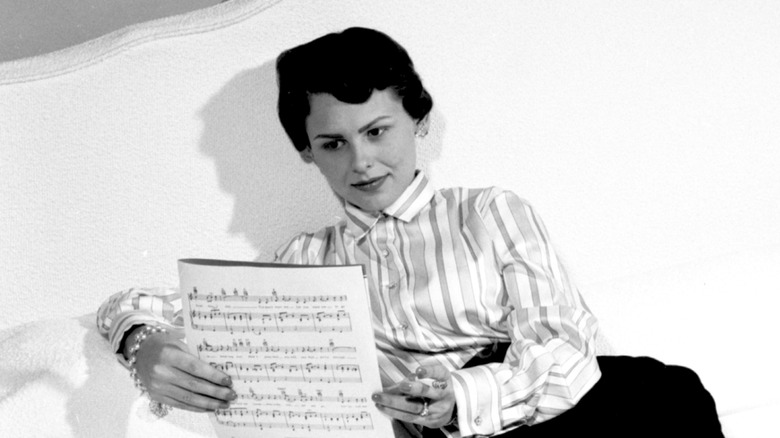 Joan Weber reading sheet music on a white bed