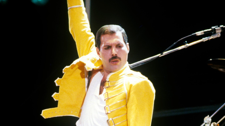 Freddie Mercury in yellow jacket thrusting arm up
