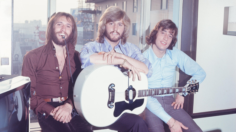 The Bee Gees posing by window with acoustic guitar and cable