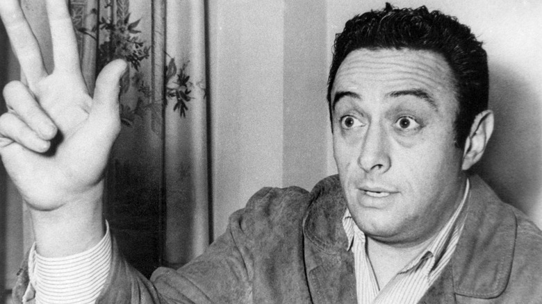 Comedian Lenny Bruce holding up hand indoors