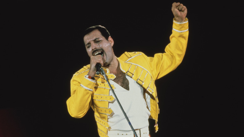 Freddie Mercury singing in yellow jacket on stage